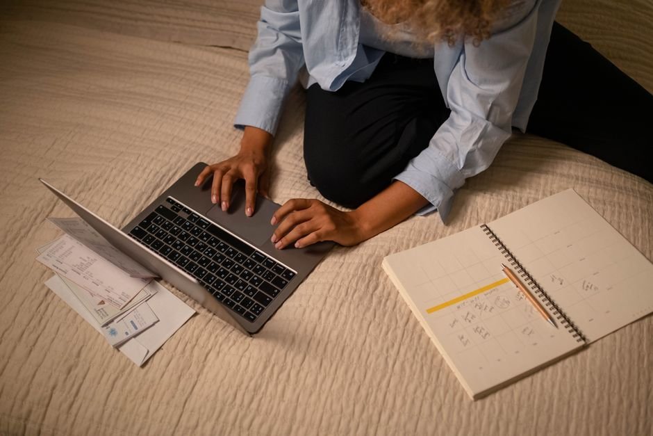 A woman working on a laptop while planning and organizing notes on a bed.