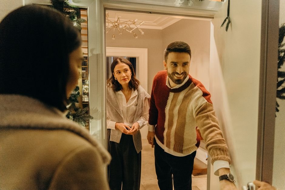 A couple greeting a guest at their doorway, capturing the warmth of a home during the holiday season.